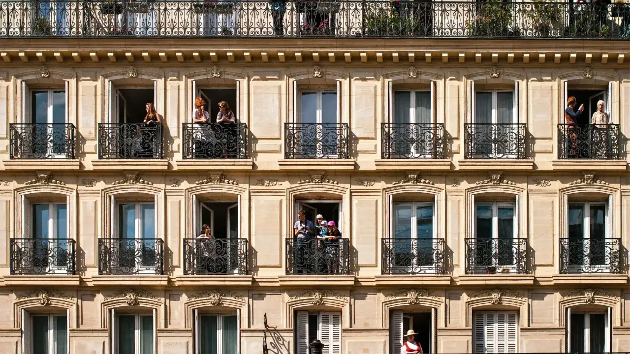 Fen&ecirc;tre ouverte sur l'architecture haussmannienne, des Parisiens profitent du soleil sur leurs balcons orn&eacute;s.
