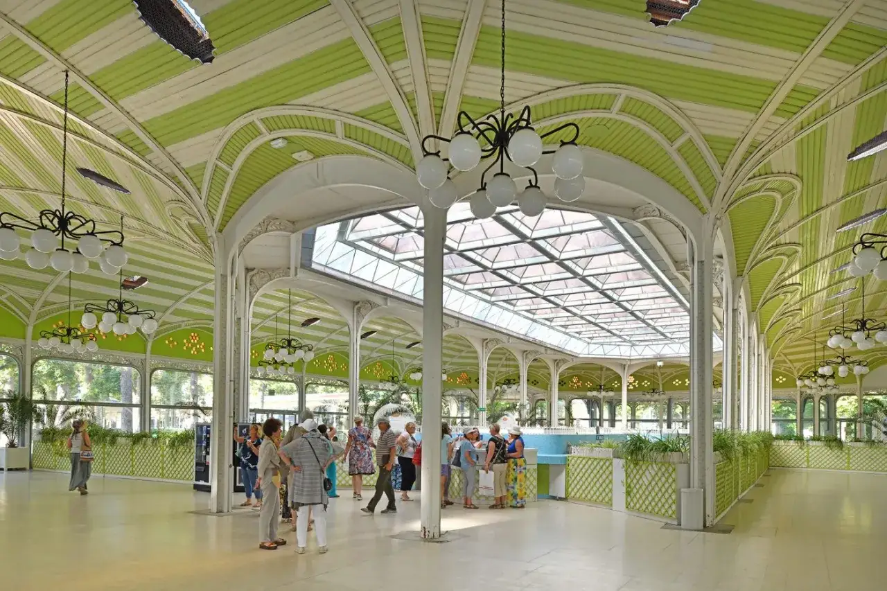 L'intérieur d'un grand pavillon orné de rayures vertes et blanches, rappelant l'élégance de la vichy histoire. Des visiteurs flânent sous les lustres.